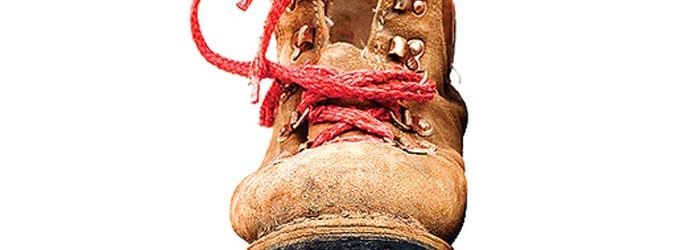 One well worn hiking book, brown with red laces on a white background