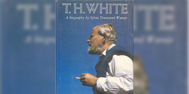 Photo of T.H. White, grey haired with a short beard, holding a cigarette against a blue sky background